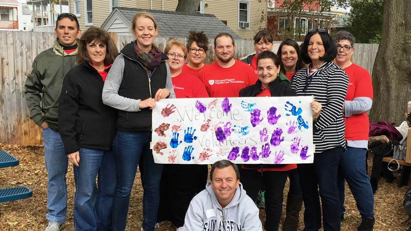 Group of employees from Harvard Pilgrim on site at Stars Preschool holding banner that says "Welcome Volunteers"